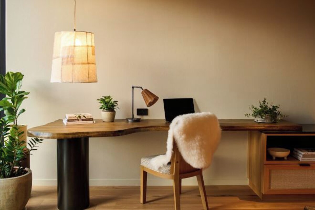 Un espacio de trabajo moderno con un escritorio de madera, una silla, una lámpara colgante y plantas en macetas.