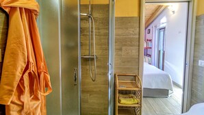 A bathroom with a glass-enclosed shower, a wicker shelf, and a bed visible through an open door. - Casa Kiwi by Interhome (Cercino)