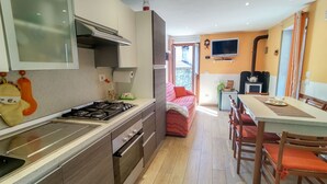 A modern kitchen with a gas stove, oven, and a dining area with a table and chairs. - Casa Kiwi by Interhome (Cercino)