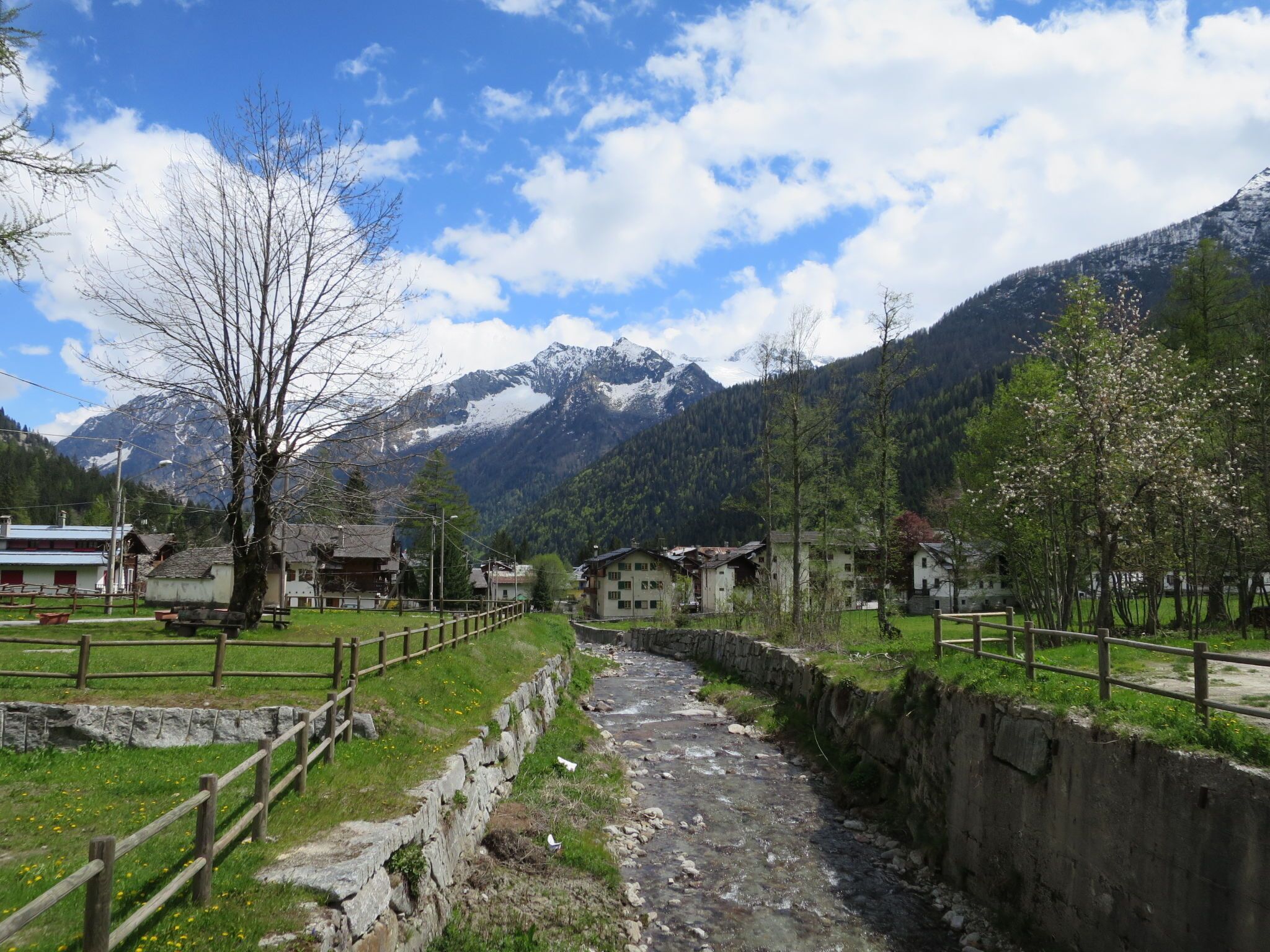 A mountain village with traditional houses, a stone wall, and a clear stream.