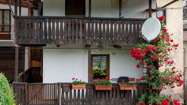Un immeuble de deux étages doté d’un balcon, d’une antenne parabolique et de fleurs rouges.