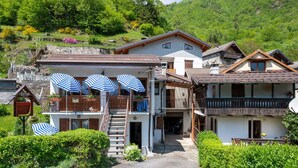 Ett traditionellt hotell i chalet-stil med en fasad av sten, träbalkonger och utomhusmöbler med randiga parasoller.