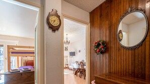 Un pasillo con piso de madera, una litera, un aparador de madera, un espejo y un reloj de pared.