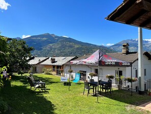 Un patio con mobiliario exterior, un paisaje montañoso de fondo y una carpa con la marca 24MX.