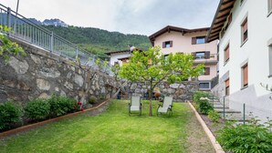 Un pati amb una paret de pedra, un arbre i una zona d'estar amb cadires.