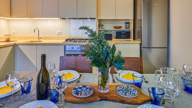 Une cuisine moderne avec des meubles blancs, un réfrigérateur en acier inoxydable et un coin repas agrémenté de verres et d’assiettes bleus.