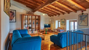 Un salon spacieux avec des poutres en bois, des canapés bleus, une bibliothèque et un téléviseur.