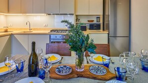 A modern kitchen with white cabinets, a stainless steel refrigerator, and a dining area set with blue glassware and plates.