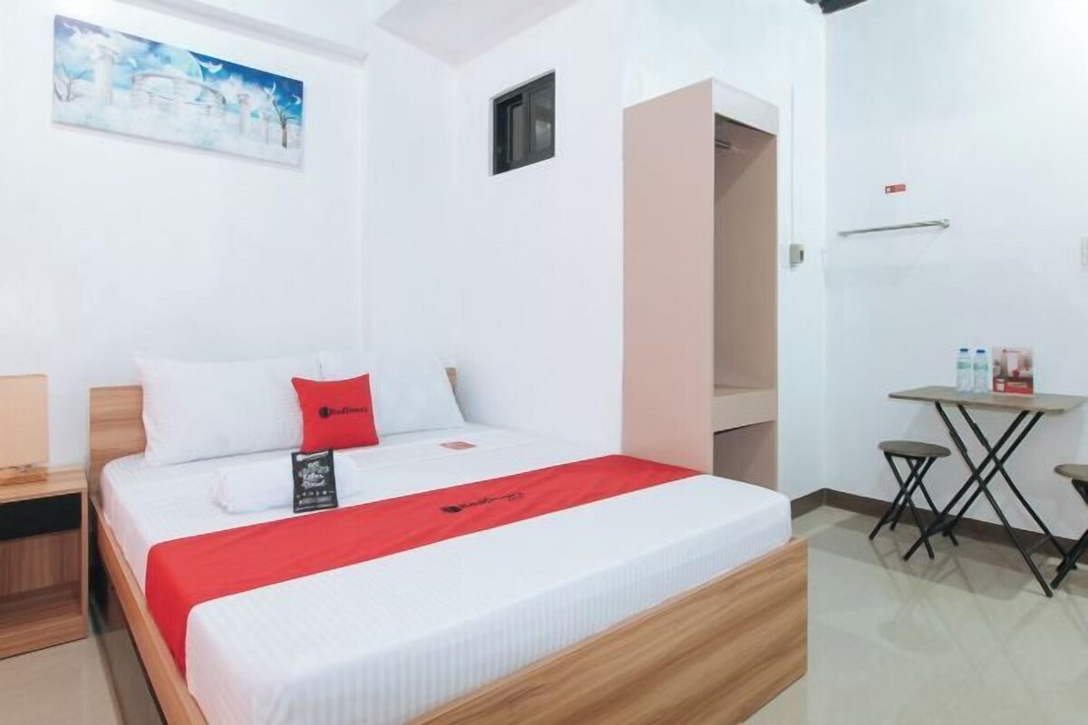 A hotel room with a bed, a small table with stools, a painting on the wall, and a door leading to another room.