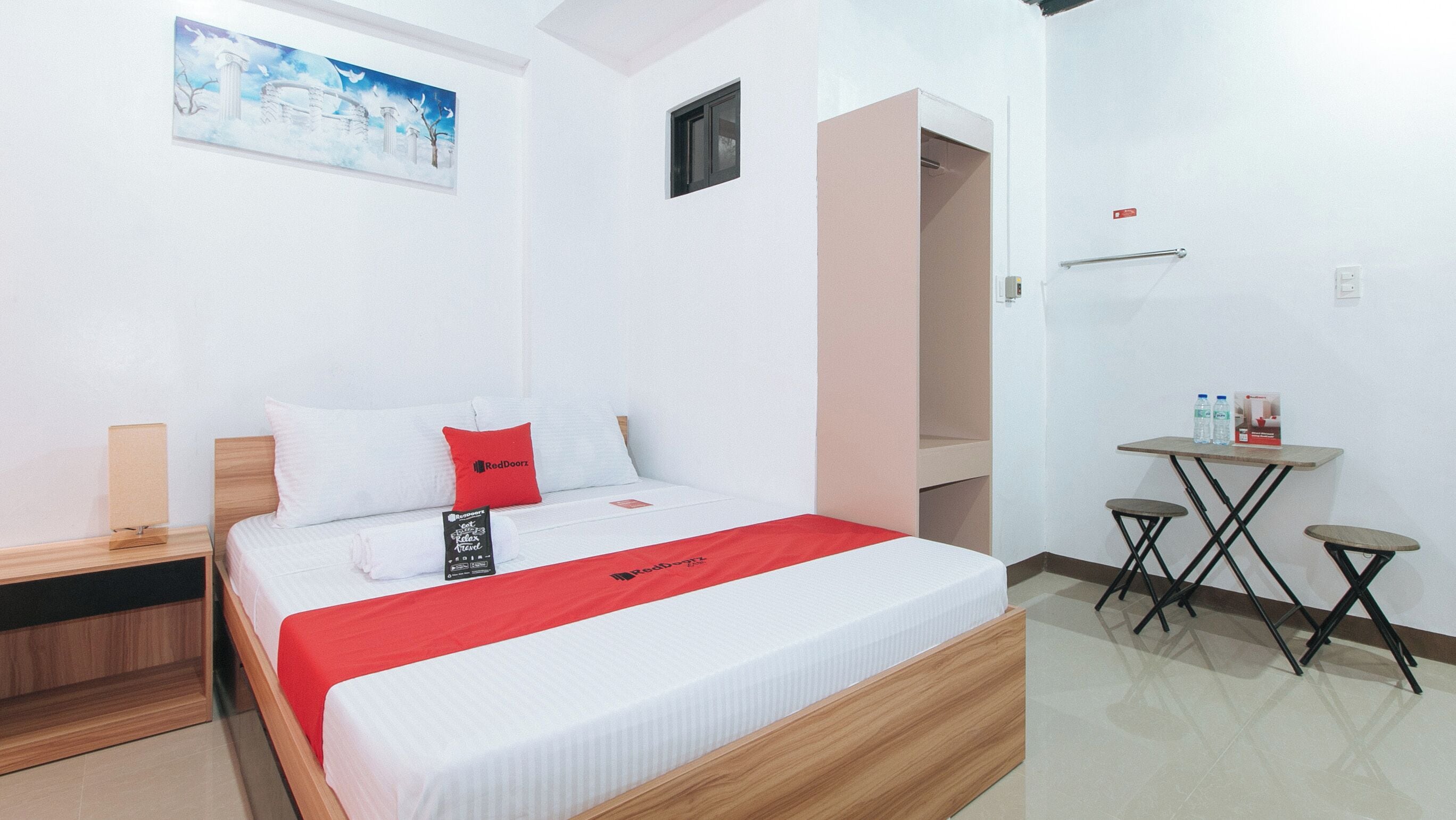 Habitación de hotel con cama, una mesita con botellas de agua, un cuadro en la pared y un armario.