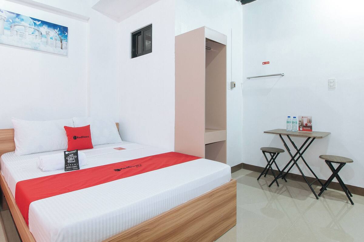 A hotel room with a bed, a small table with water bottles, a painting on the wall, and a closet.
