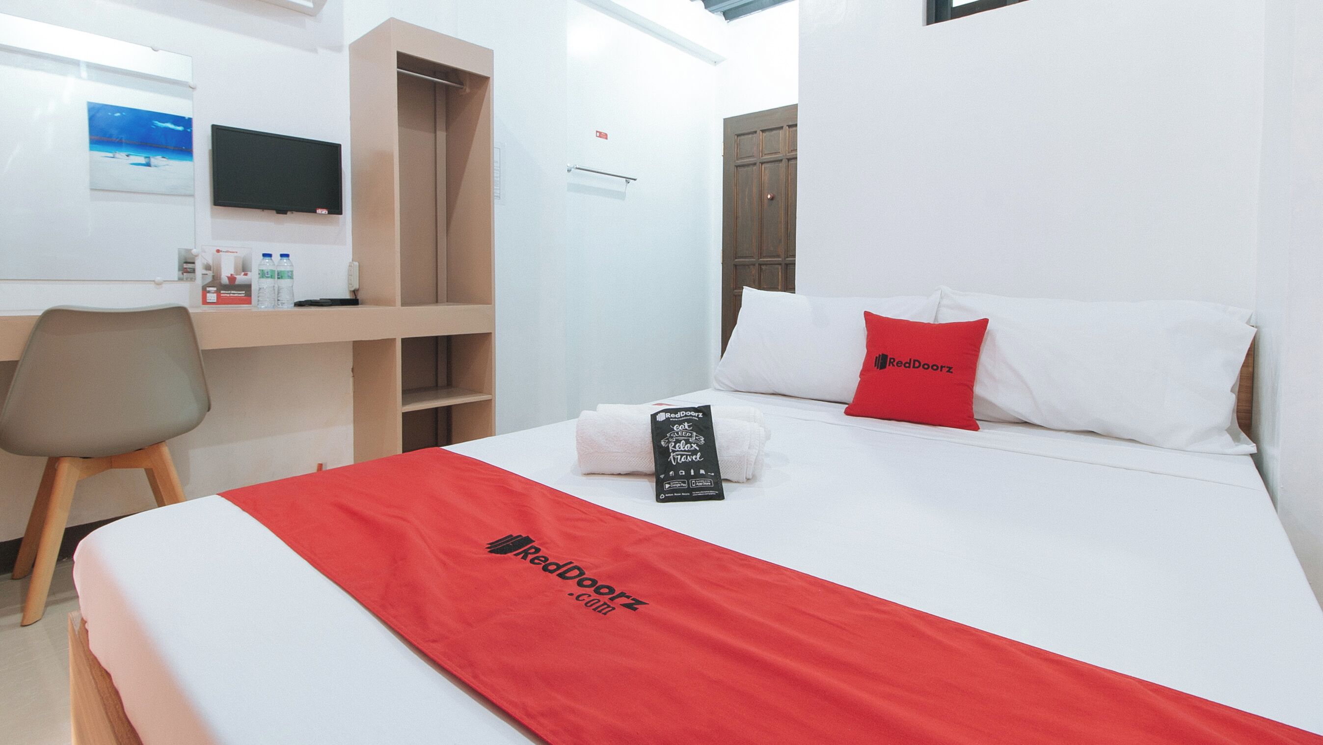 Una habitación de hotel con una cama, un escritorio, una silla y un televisor en la pared.