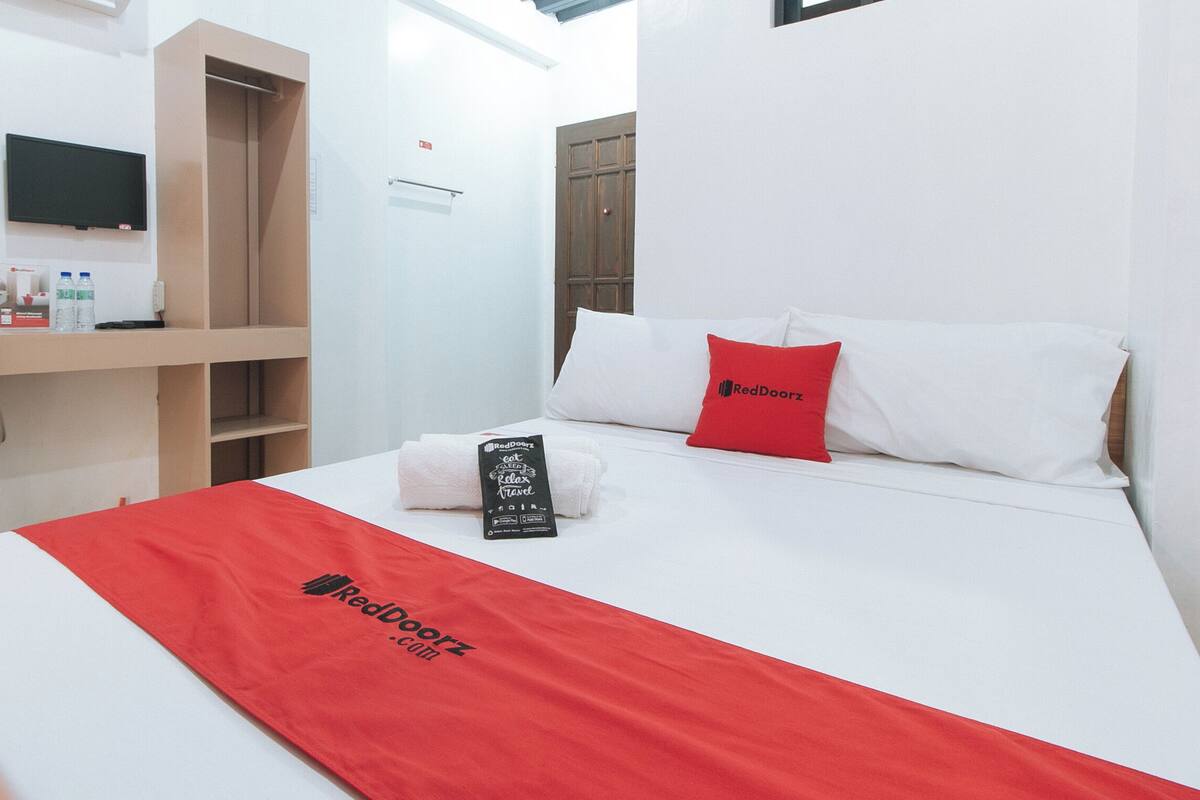 A hotel room with a bed, a desk, a chair, and a TV on the wall.