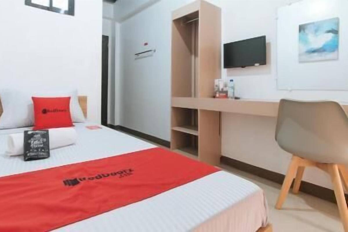 A hotel room with a bed, a desk, a chair, and a TV on the wall.