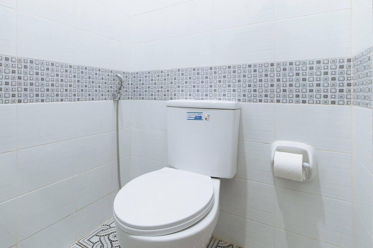 A bathroom with a toilet, a toilet paper holder, and patterned tiles on the walls.