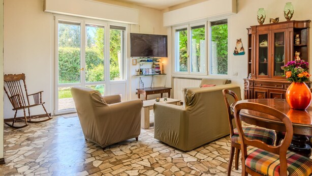 Un vaste espace de vie doté d’un sol carrelé en pierre, d’un téléviseur fixé au mur et d’une table à manger avec des chaises.