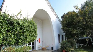 Un bâtiment blanc doté d’une arche incurvée, d’un escalier en pierre menant à une porte, d’un espace extérieur aménagé pour s’asseoir et de plantes en pot.