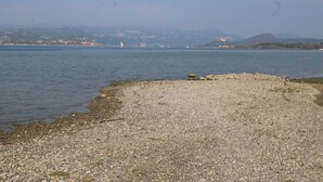 Une plage de galets offrant une vue sur une ville lointaine et des montagnes.