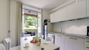A modern kitchen with white cabinets, a stainless steel refrigerator, and a dining area with a table set for two. - Fon 105 by Interhome (Fondotoce)