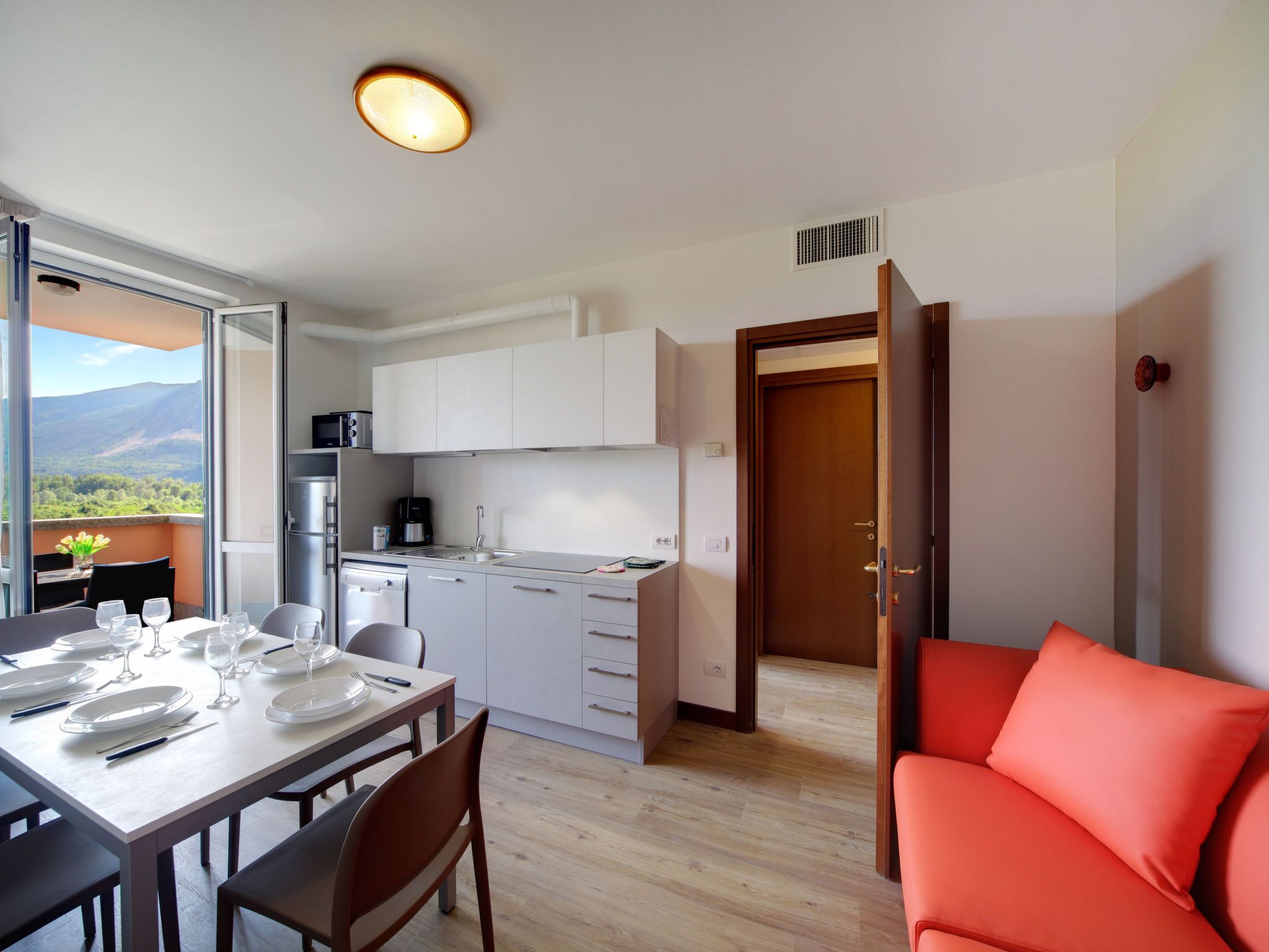 A modern kitchen with white cabinets, a dining area with a table set for four, and a view of the outdoors.