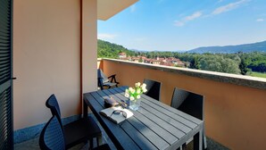 Uma varanda com mesa, cadeiras e vista para uma cidade e colinas.