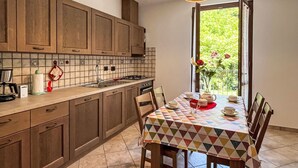 Een keuken met houten kastjes, een betegelde achterwand en een eettafel met een kleurrijk tafelkleed.