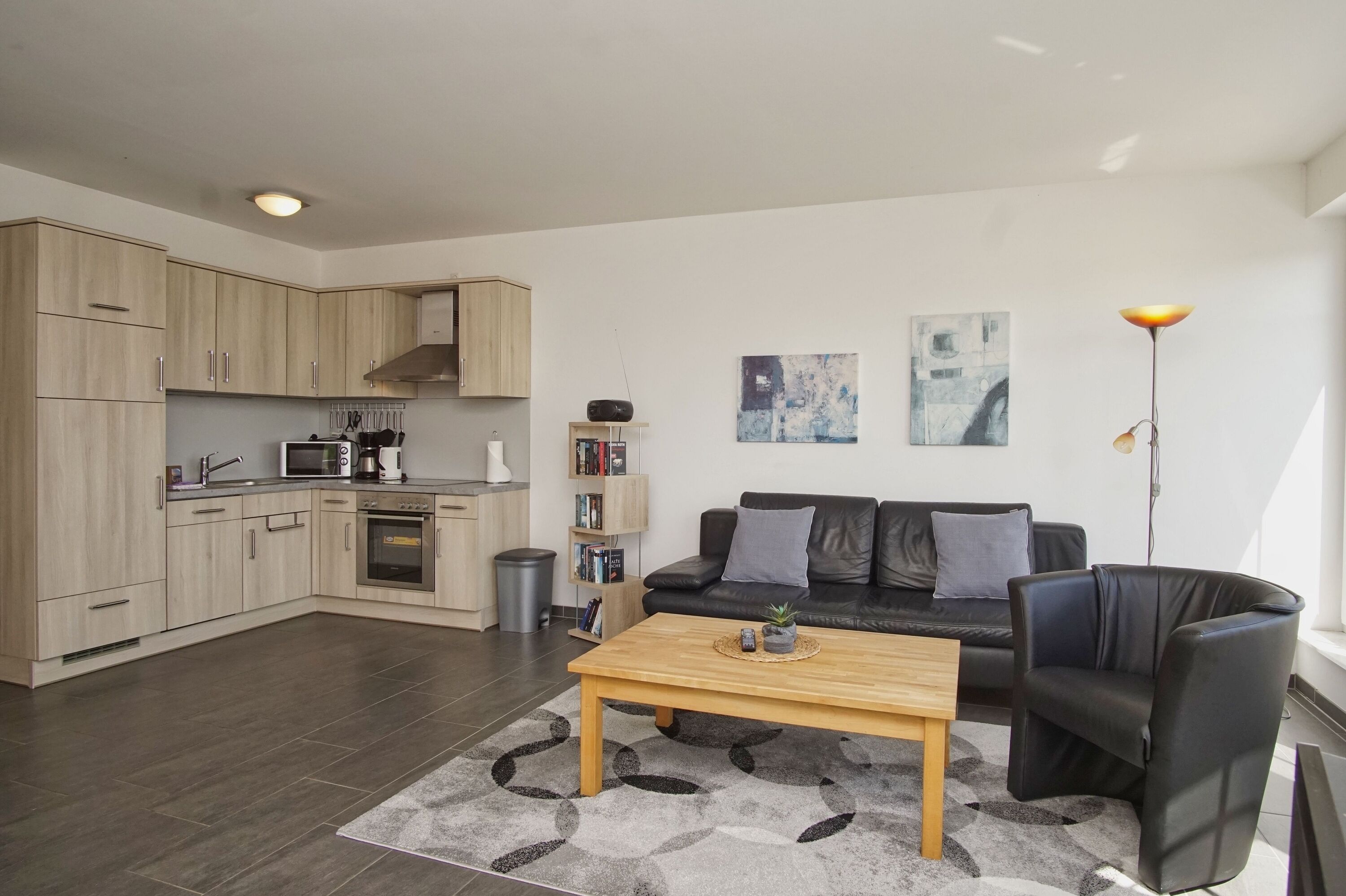 A modern kitchen with built-in appliances, a black leather sofa, a wooden coffee table, and abstract art on the walls.
