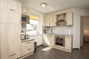 Une cuisine moderne avec des meubles en bois clair, des appareils en acier inoxydable et une fenêtre équipée de stores.