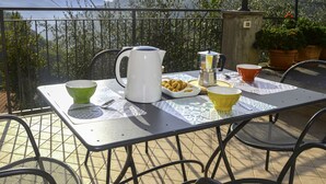 A terrace with a table set for breakfast, overlooking a mountainous landscape.