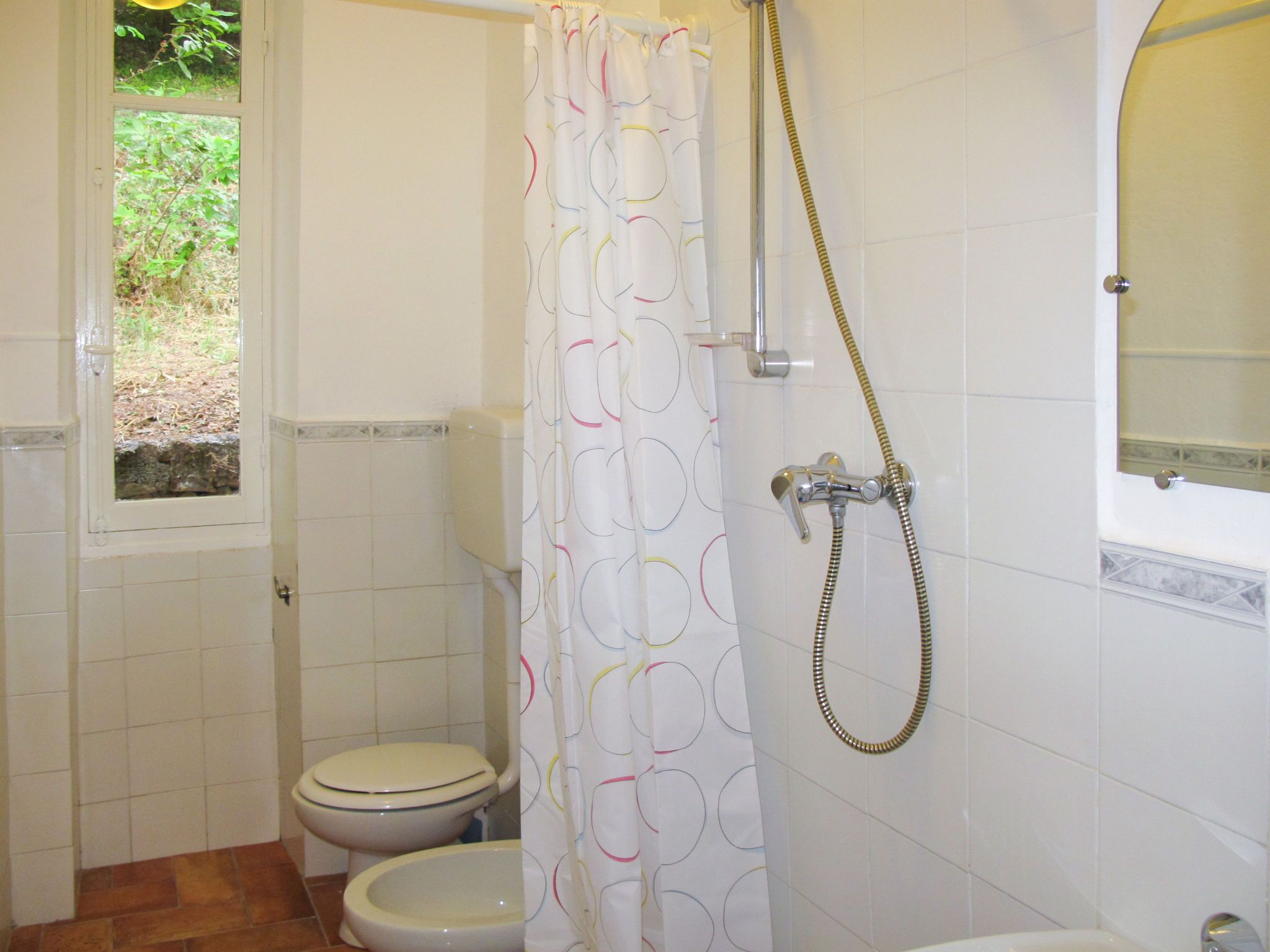 Een badkamer met twee toiletten, een douche en een raam met uitzicht op groen.