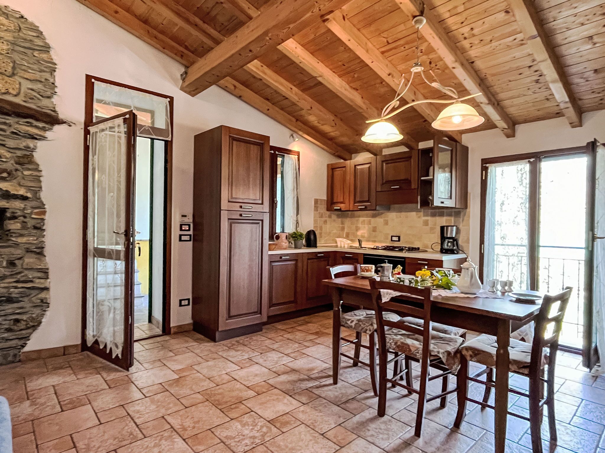 A rustic kitchen with wooden cabinets, a dining table with chairs, and a stone wall.