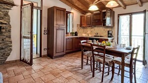 A rustic kitchen with wooden cabinets, a dining table with chairs, and a stone wall. - Ca' da Prima Porta (VLO131) by Interhome (Valloria)