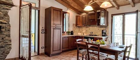 A rustic kitchen with wooden cabinets, a dining table with chairs, and a stone wall.