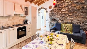 Une cuisine chaleureuse avec un mur en pierre, un plafond en bois et un coin repas où une table est dressée pour deux personnes.
