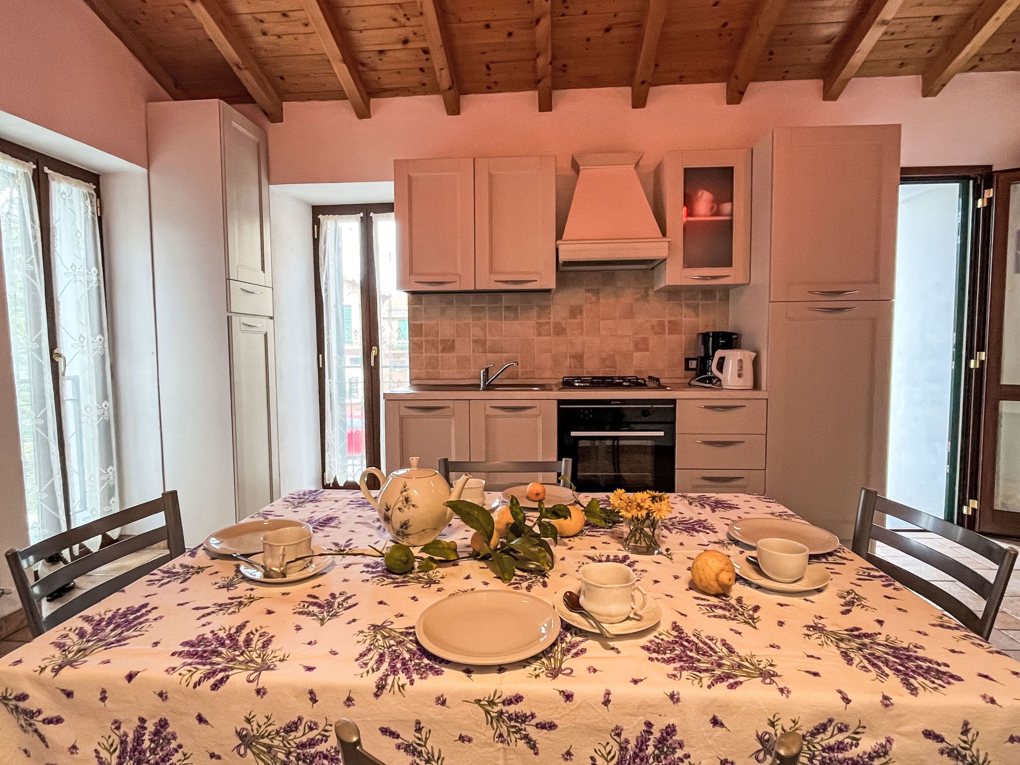 A dining area with a table set for four, surrounded by wooden chairs. A kitchen with modern appliances and cabinets is visible in the background.