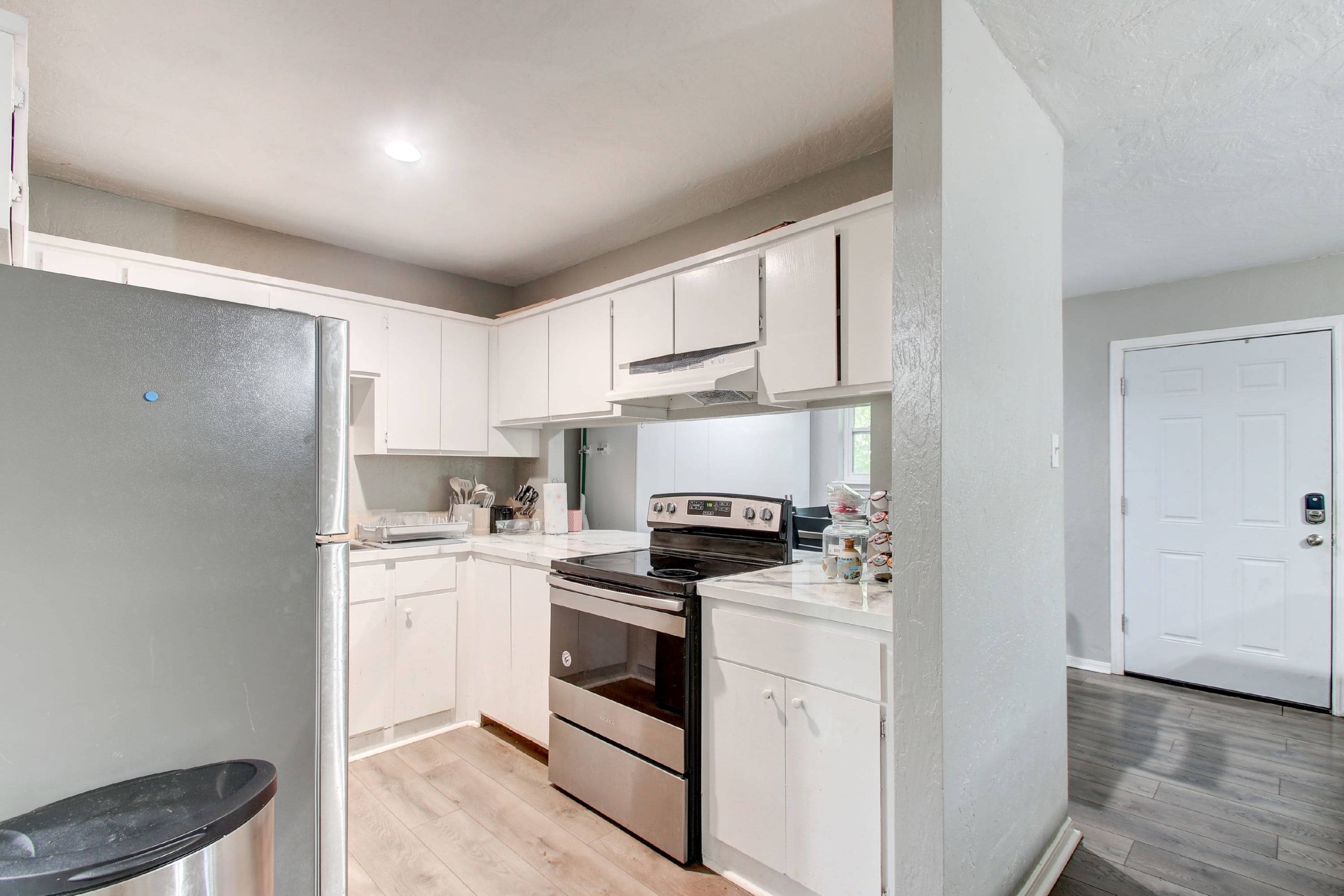 A modern kitchen with white cabinets, stainless steel appliances, and a wooden floor.