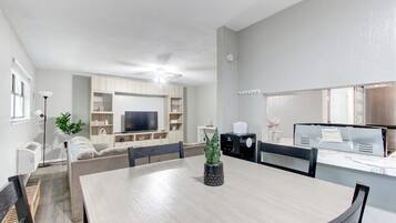 Un salon moderne comprenant une table à manger, des chaises, un canapé, un téléviseur et un coin cuisine équipé d’un four à micro-ondes et d’un grille-pain.