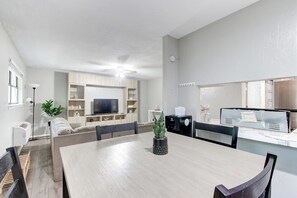 Una sala de estar moderna con una mesa de comedor, sillas, un sofá, un televisor y una zona de cocina con microondas y tostadora.