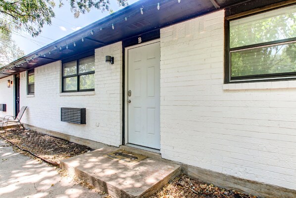 A white brick building with a white door marked 'B', a window, and a small porch area.