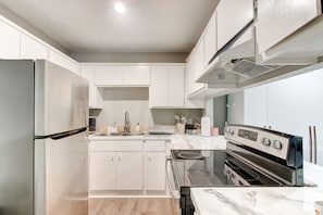 A modern kitchen with white cabinets, a stainless steel refrigerator, a black stove, and a marble countertop. - Cozy 2 Bedroom Apartment in Lawton Near Downtown (Lawton)