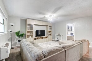 Una sala de estar moderna con un sofá modular, un televisor de pantalla plana, estanterías empotradas, un ventilador de techo y un radiador.