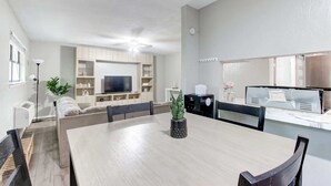 Ein modernes Wohnzimmer mit Esstisch, Stühlen, einer Couch, einem Fernseher und einer Küchenzeile mit Mikrowelle und Toaster.