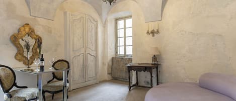 A room with a bed, a desk with chairs, a chandelier, and a large mirror.