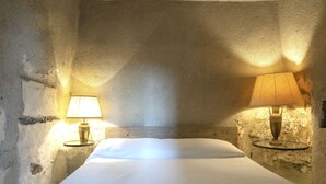Un lit simple avec une tête de lit en bois, dans une pièce aux murs texturés et agrémentée de deux lampes de chevet.