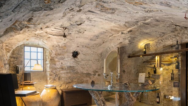 Un intérieur rustique avec des murs en pierre, une table ronde en verre, un banc en bois et un grand vase.