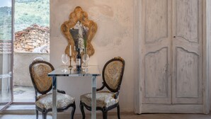 Un coin repas avec une table dressée pour deux personnes, un miroir et une vue sur un mur de pierre et la verdure à l’extérieur.