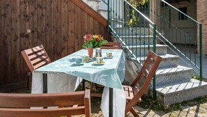 Una mesa de comedor al aire libre con sillas, una planta en maceta y una escalera con barandilla de metal.