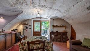 Uma cozinha rústica com armários de madeira, uma mesa de jantar com toalha de mesa estampada e uma sala de estar aconchegante com sofá e lareira.