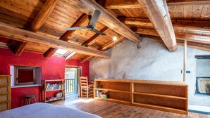 Quarto com uma cama grande, vigas de madeira no teto, uma estante e uma parede vermelha.