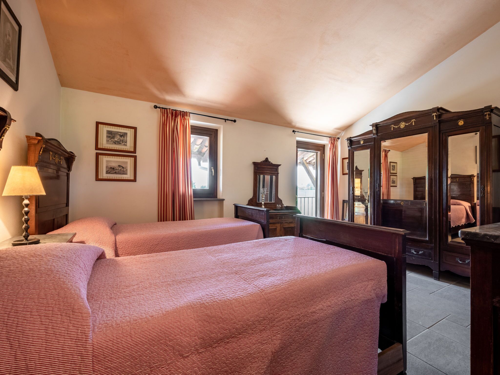 A room with two beds, a wooden dresser, a mirror, and a window with curtains.
